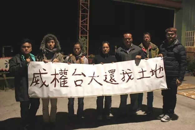 一群人在夜晚舉著標語，表達對土地權益的訴求。