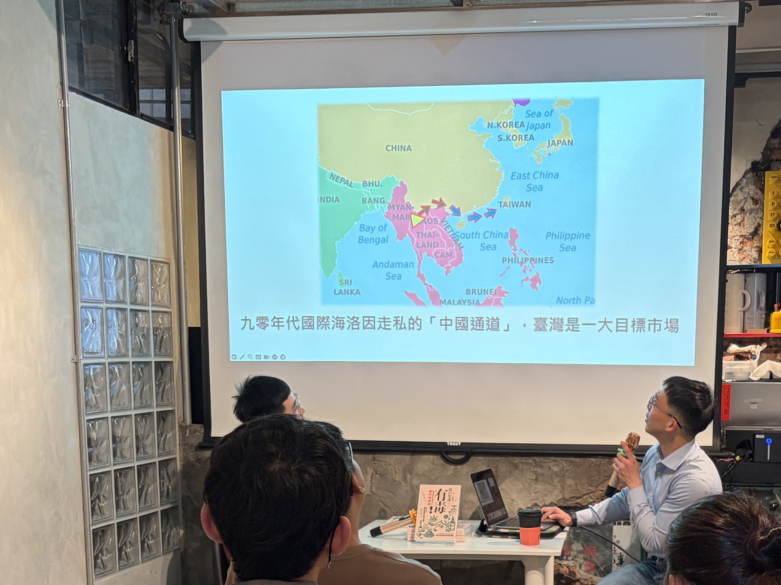 A group of people sitting in a seminar room, watching a presentation on a screen that displays a map of East Asia, while a speaker discusses the topic.