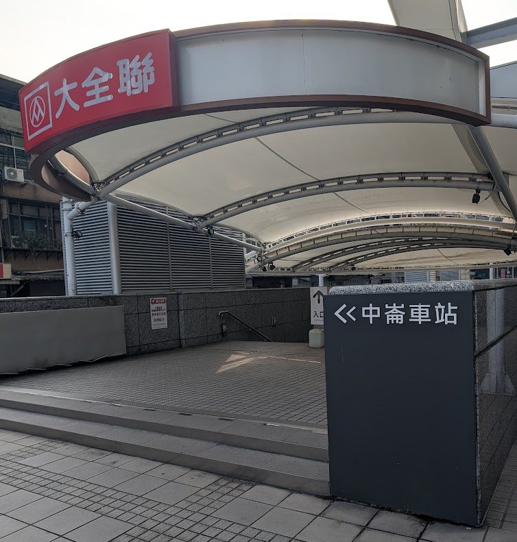 捷運中壢車站的出入口,標誌清晰可見,周圍有遮陽篷設施。