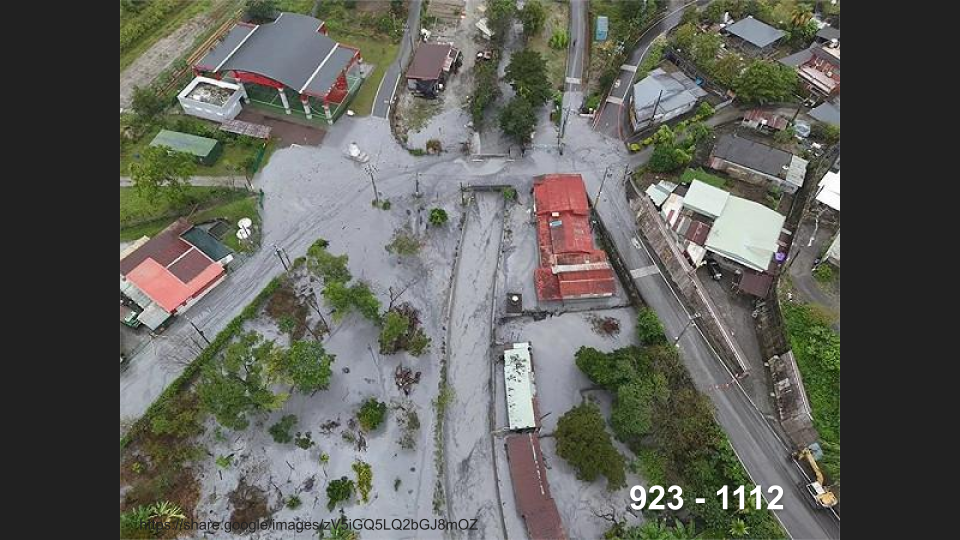 從空中俯瞰的村莊，周圍被灰色火山灰覆蓋，住宅和道路清晰可見。