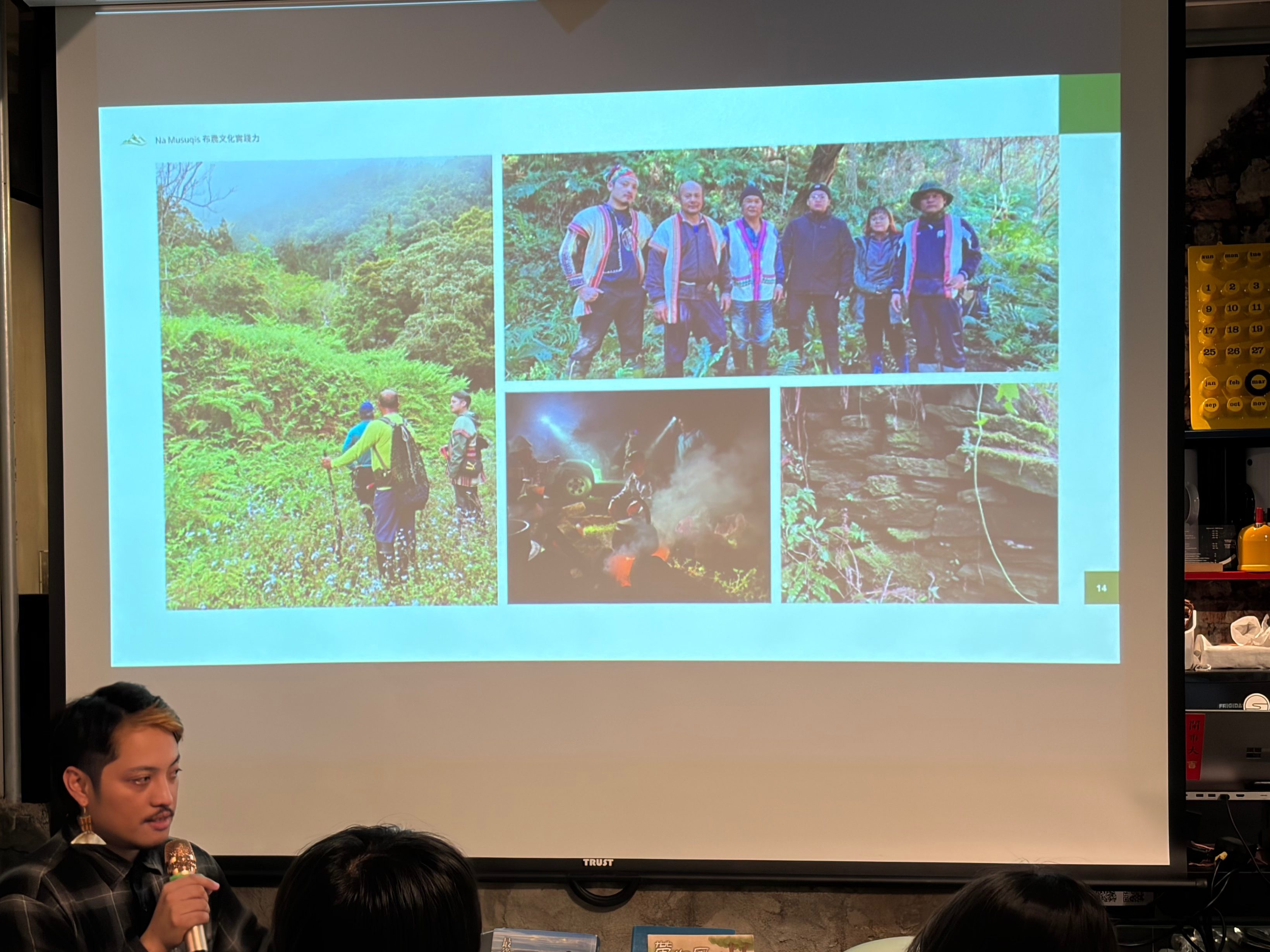 一位男性正在講話,背景是一個展示屏幕,顯示有關登山的圖片,包括登山者和自然風景。